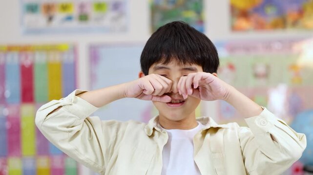 Young Asian Boy Crying and Rubbing Eyes in a Classroom Setting