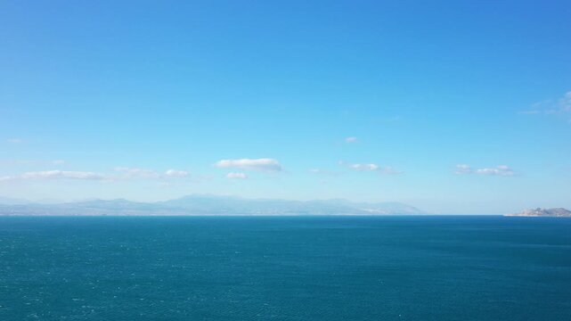Wide view of the deep blue sea with distant mountains and coastline under a clear sky near Corinth, Greece. Tranquil seascape ideal for travel and nature concepts.