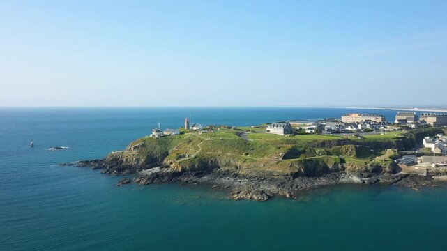 Scenic aerial view of Pointe du Roc with rocky coastline, lighthouse, and buildings overlooking the blue sea under a clear sky in France.