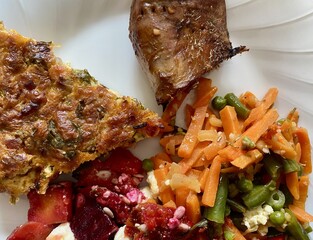 Quiche, vegetables, beetroot salad and roasted pork belly on a plate