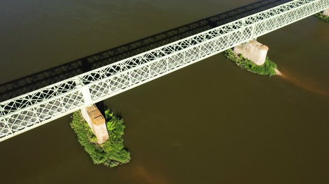 Drone shot of a lattice metal bridge crossing the Loire River near Sully sur Loire, France, with green supports and calm water below.
