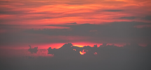 Dramatic sunset with fiery red sky and dark clouds creating a beautiful natural light display in...