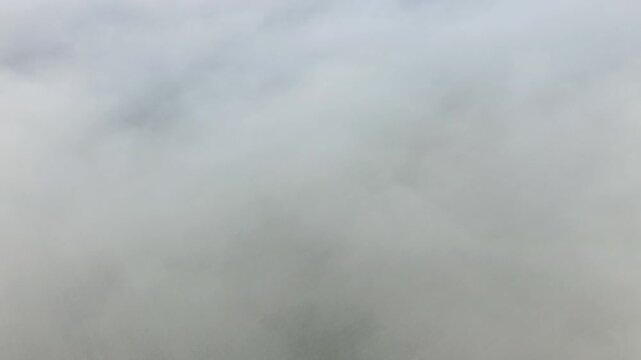 Aerial view of thick fog covering the rural landscape in the Loiret region, creating a soft and mysterious atmosphere. The mist obscures most ground details, offering a tranquil and ethereal scene.