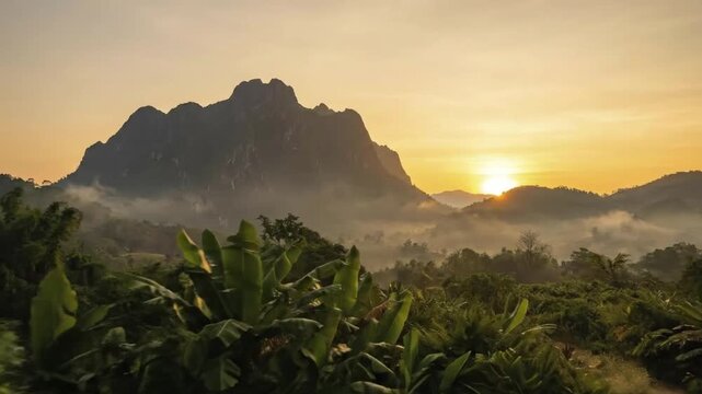 A breathtaking sunrise or sunset illuminates a majestic mountain landscape, casting a radiant golden glow across the vast sky. Layers of soft, ethereal mist gently drift and settle within the valleys 