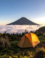 Camping at dawn with tent and majestic mountain piercing clouds