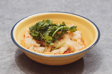 A yellow bowl filled with fish fillet salad garnished with fresh coriander and chili slices.