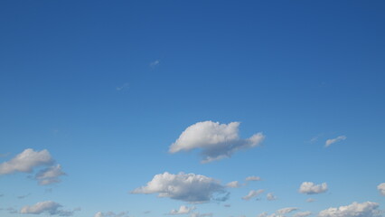 A beautifully clear blue sky adorned with fluffy white clouds drifting gently across it