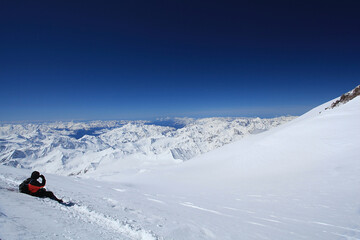 High altitude winter landscape with mountaineer sitting on snow slope, panoramic view of endless...