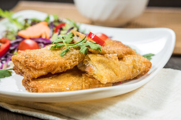 Golden-brown fried bean curd rolls served on a white plate with fresh coriander and chili garnish.