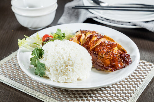 A white plate featuring roasted chicken slices served with steamed white rice and fresh salad garnish.