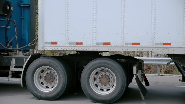 POV Close up of a semi-truck wheels, axle, fuel tank, and chassis in motion. Detailed view of heavy-duty trucking mechanics and industrial transport on the road.