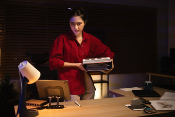 Interior designer holding material catalogs while working overtime at night in a cozy home office, wondering if it&rsquo;s time to finish work