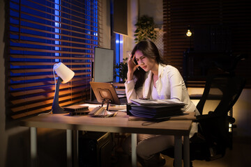 Tired architect holds her head while working on building extension plans under warm desk light at night
