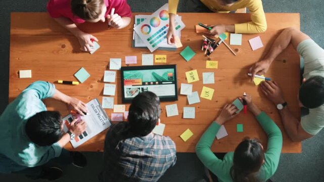 Top view of business people working together to design web design. Aerial view of designer brainstorming and discussing about website interface and looking at tablet with digital design. Symposium.
