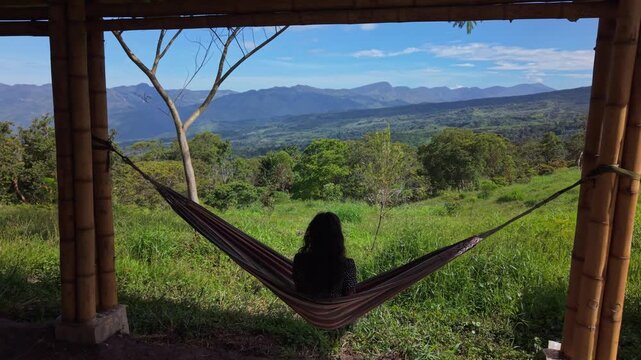 Slow-moving drone flies forward over a girl resting in hammock, transitioning into expansive view of Colombia&rsquo;s lush green mountains, creating first-person feeling of openness calm immersion in nature