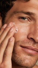 Obraz premium Young man applying moisturizing cream on his cheek, hydrating and protecting facial skin for a healthy glow, representing daily male grooming and self care routine