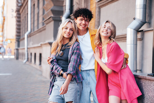 Group of young three stylish friends posing in the street. Fashion man and two cute female dressed in casual summer clothes. Smiling models having fun. Cheerful women and guy outdoors