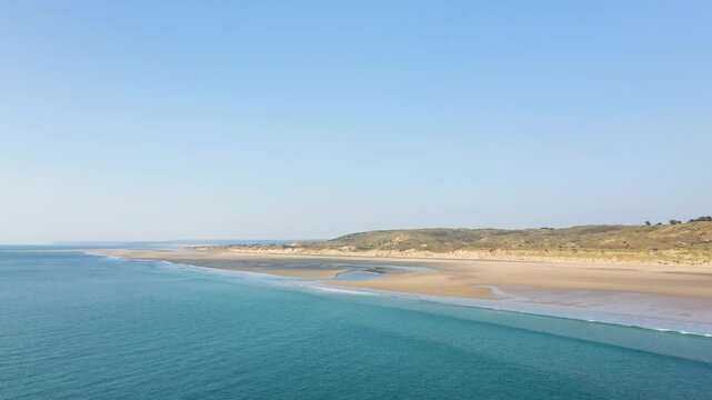 Aerial view of the expansive sandy shoreline and turquoise waters at Plage de la Vieille eglise under a clear blue sky. The tranquil coastal landscape features gentle waves and natural dunes.