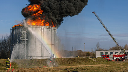 A large oil tank at an oil refinery is on fire. Firefighters extinguish a fire at an oil depot caused by an oil storage tank fire. A fire truck extinguishes a burning oil tank.