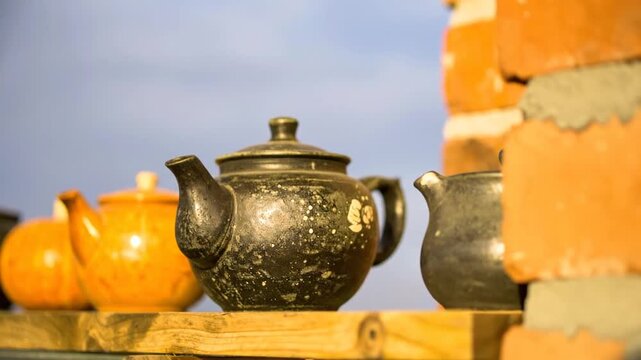A row of ceramic teapots, various colors, on a wooden shelf, brick wall background