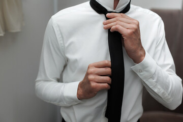 Man adjusts black tie while dressing in formal white shirt for an elegant event or occasion in a modern setting