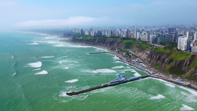 Sunny morning Miraflores Barranco Barranquito Playa Makaha beach pier aerial drone Lima Peru clear hazy blue skies residential skyscraper buildings cars traffic highway ocean view surf waves static