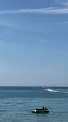 Naklejka premium Jet ski on a calm blue sea under a clear blue sky. Peaceful seascape with minimal composition, travel and summer vacation concept, vertical photo with copy space