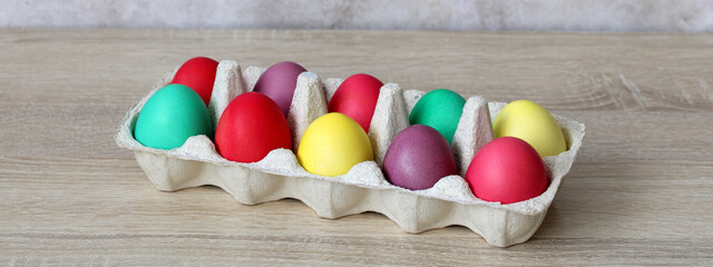 Colorful easter eggs in carton on wooden table