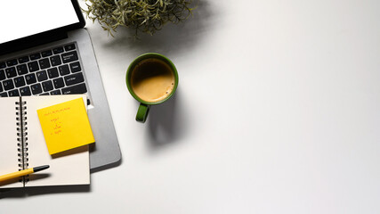 Office desk table with blank notebook, laptop, supplies and coffee cup. Top view with copy space. Flat lay.