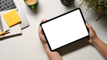 Woman hand holding tablet on office desk workspace with, pen, laptop, flower and hot coffee cup on white table