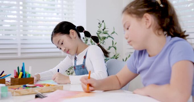 asian girl elementary student drawing with pencil during slow motion classroom education activity caucasian girl classmate works on art project teamwork friendship creativity childhood study learning
