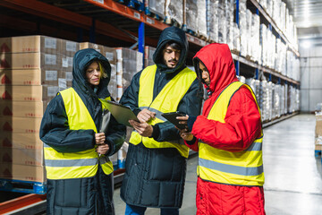 Team of diverse workers checking inventory and using digital tablet in a low temperature cold storage logistics warehouse