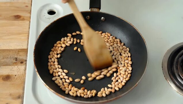 High resolution 4K top view footage of wooden spatula stirring pine nuts on frying surface highlighting texture motion culinary preparation food focused stock 