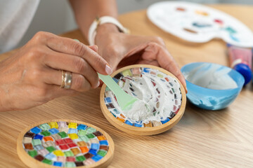 DIY arts and crafts hobby. Female hands sealing coaster surfaces with a fixator layer to complete their finish. Shows material awareness, smooth application, and thoughtful craft practice.