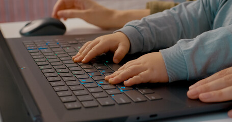 Close-up of a baby's hands eagerly typing on a laptop keyboard while a parent works in a home...