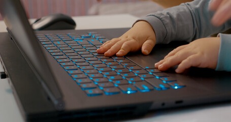 Baby's hands eagerly tap on a laptop keyboard while the mother works in her home office, showcasing...