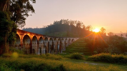 Obraz premium Majestic Sunrise Over Historic Bridge Surrounded by Lush Greenery and Rolling Hills in a Serene Landscape