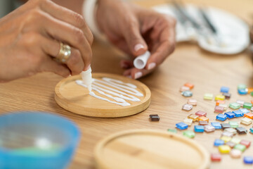 Woman using glue to assemble coaster components at home. Shows controlled placement, material awareness, and patient creative work.