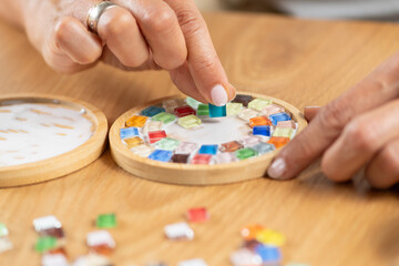 Female hands assembling coasters by gluing small decorative parts during a home craft session. Highlights precision, hand coordination, and detailed creative work.