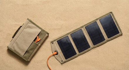 Fototapeta premium Foldable portable solar panel charger with orange cable on a textured beige background in a minimalist flat lay.