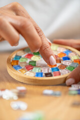 Arts and crafts hobby. Placing and gluing tiny decorative parts on coaster surfaces at home. Highlights careful artistry, measured technique, and slow craft rhythm.