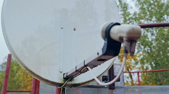 Focused satellite receiver head showing aged broadcast technology in rain