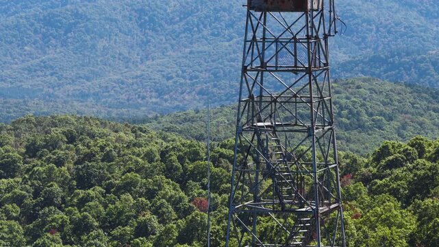 Devils Knob fire lookout tower surrounded by dense lush green forest canopy, aerial telephoto pullback establish