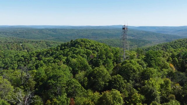 Wide aerial pullback of forested hills and distant ridgelines near Devils Knob Lookout in Arkansas, tower on right third