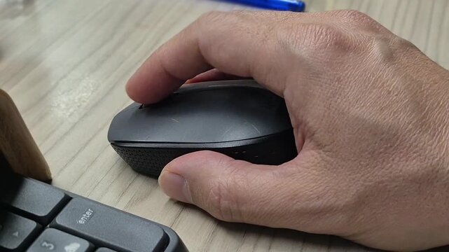 A computer user is playing with a computer mouse. We only see the hand. It is performing various movements with the mouse. Close-up. No people. Part of the keyboard is visible.
