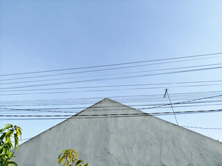 Residential roof intersected by overhead electric cables under blue sky, suitable for urban lifestyle and infrastructure concepts.