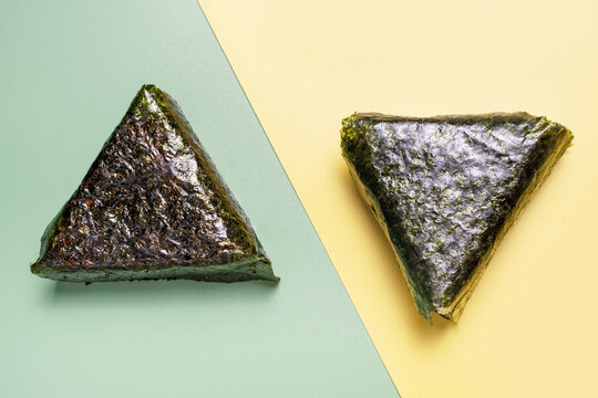 Two triangles of nori with rice on a green and yellow background, close-up, top view