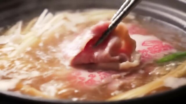 Close up of cooking meat in broth with steam and chopsticks