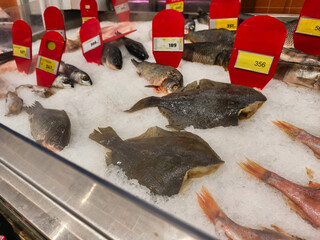 Fish on display. A variety of fresh seafood, including whole flounder, perch, and red mullet, is displayed on crushed ice with red price tags at a supermarket or fish market.