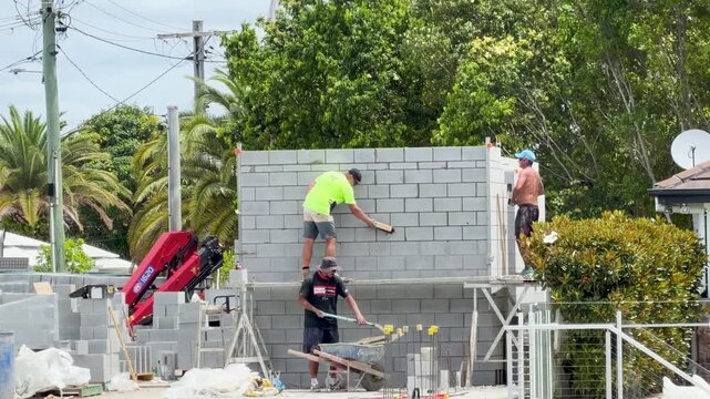 Construction workers building concrete block wall in suburbia